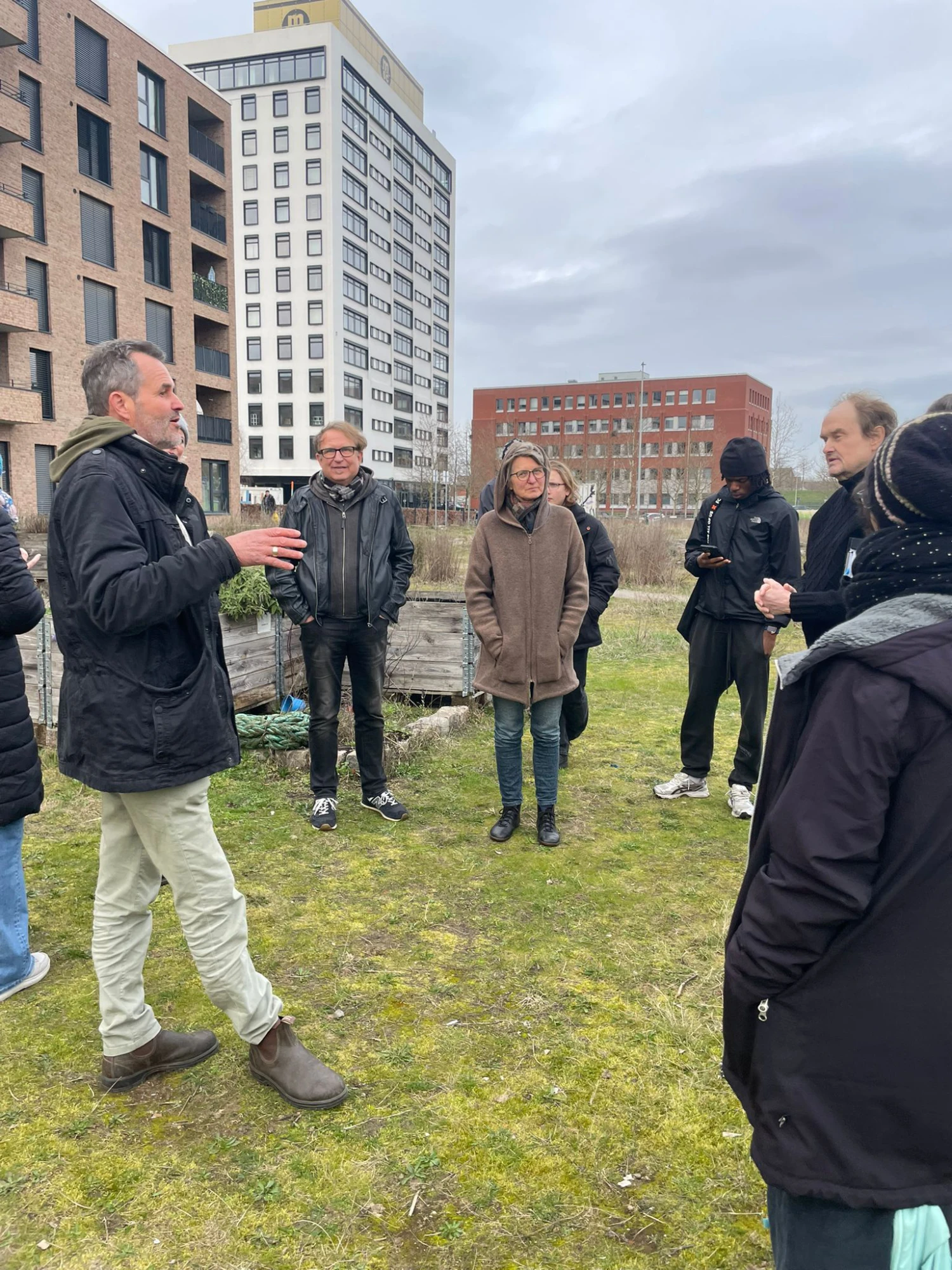 zu sehen ist die Überseewiese mit Hochbeeten. Dazwischen stehen die Menschen, die bei der Begehung teilnehmen.