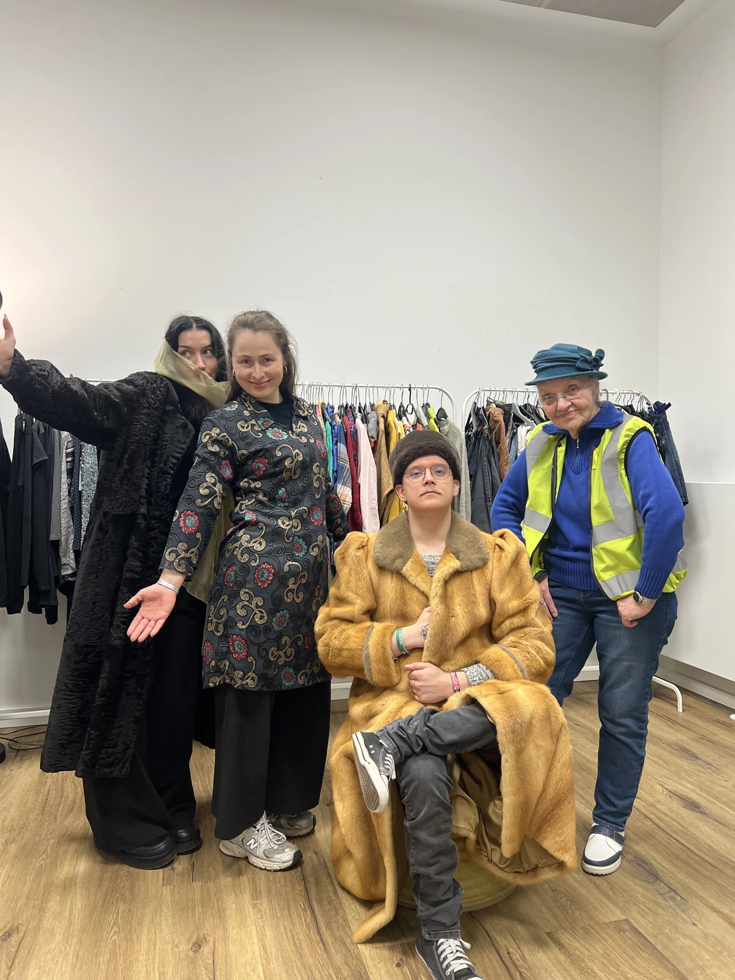Mehrere Personen die Kleidung vom Kleidertausch tragen und damit posieren. Darunter ist Kleidung wie ein Fellmantel, ein blauer Filzhut und eine gelbe Warnweste.