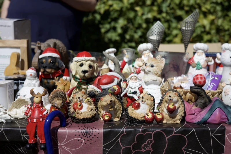 Tisch mit verschiedenen Weihnachtsfiguren und Tierfiguren aus Keramik oder Stoff, darunter Igel, Hunde mit Weihnachtsmützen, ein Weihnachtsmann und ein Rentier in rotem Pullover