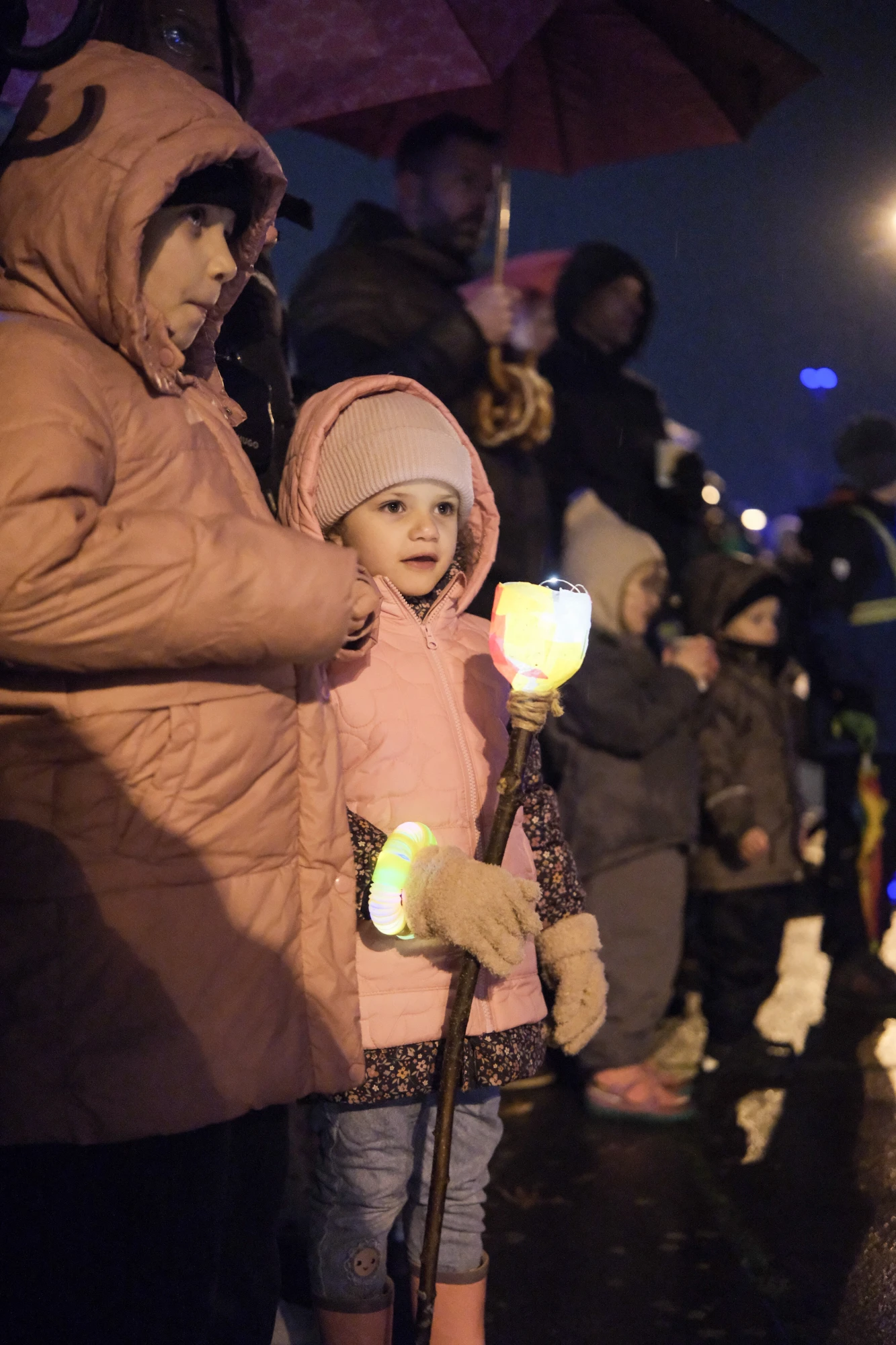 Mehrere Kinder in Winterkleidung halten leuchtende Laternenstäbe bei Nacht im Freien.