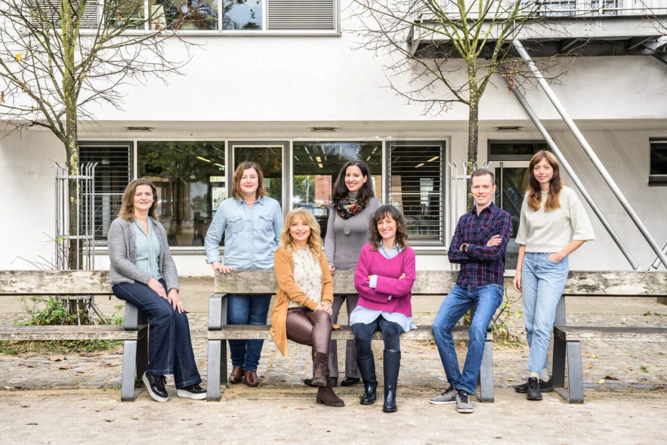 Sieben Personen stehen vor dem Quartierszentrum Morgenland in Gr&ouml;pelingen. Sie stehen versammelt um B&auml;nke herum und lachen in die Kamera. Es ist das Team der Bildungsberatung in Gr&ouml;pelingen.