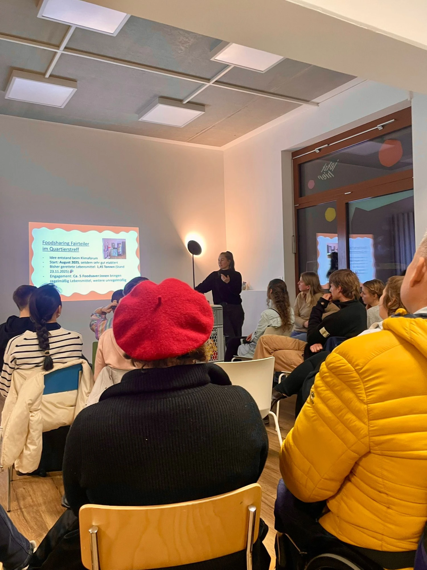 Zu sehen ist ein Publikum von hinten, das nach vorne auf eine Beamer Projektion schaut