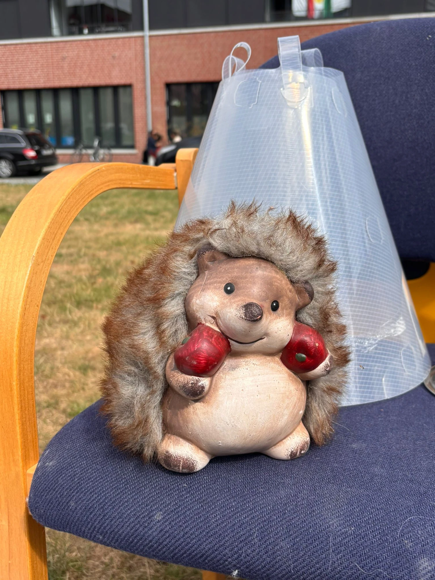 Figur eines Igel mit roten Äpfeln in den Pfoten und Fellrücken sitzt auf blauem Stuhl mit Holzarmlehne vor transparentem Kunststofftrichter