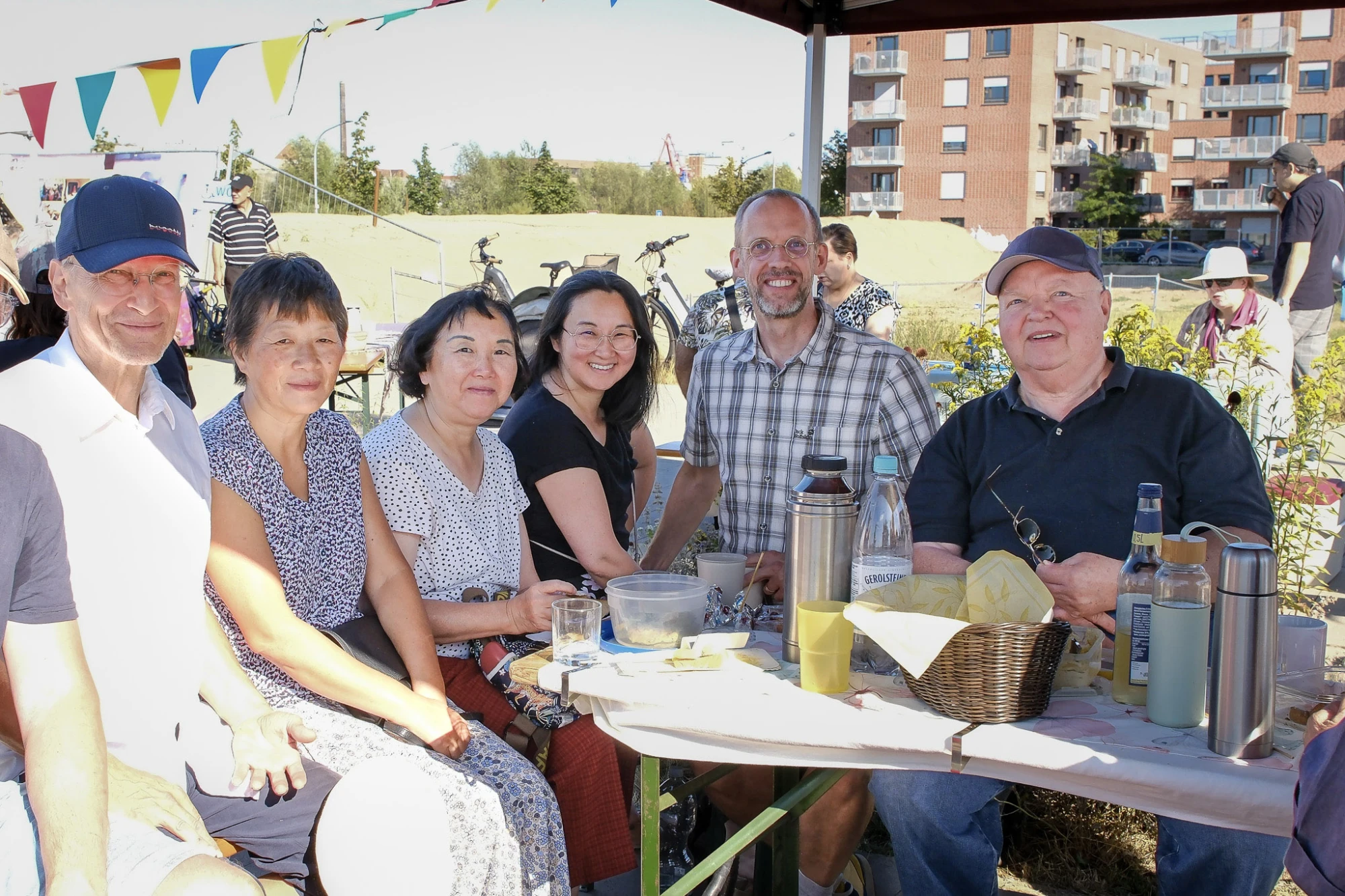 Sechs Personen sitzen im freien unter einem Pavillon an einem Picknicktisch und unterhalten sich.