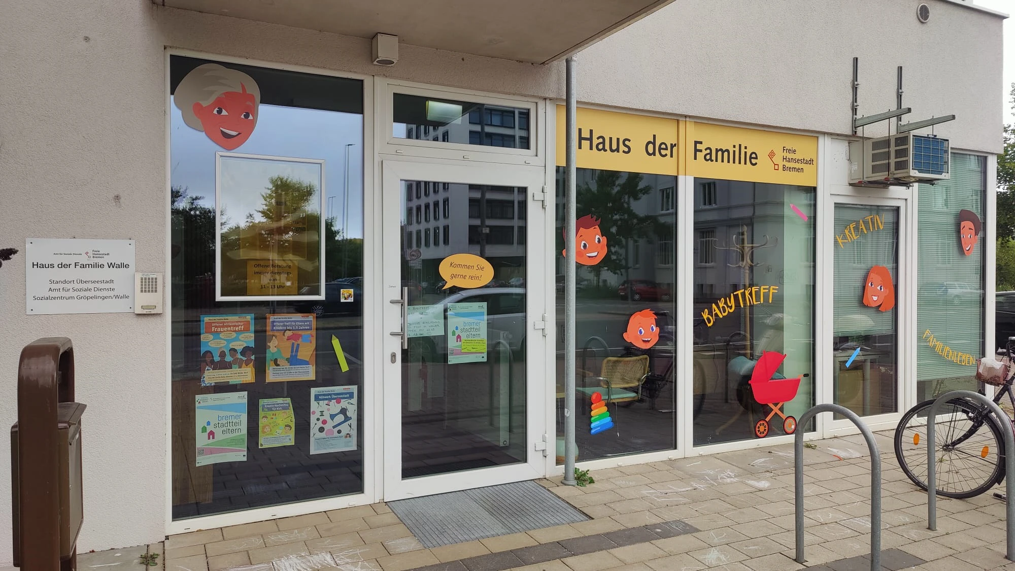 Eingang eines Hauses mit Glasfront und Aufklebern von lachenden Gesichtern sowie dem Schriftzug 'Haus der Familie'